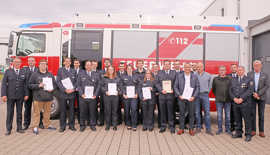 Männer und Frauen in Feuerwehr-Uniform stehen vor einem roten Löschfahrzeug