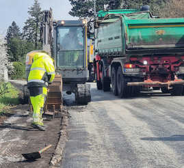 Baumaschinen und ein Arbeiter im Einsatz bei der Instandsetzung einer Straßenfahrbahn.