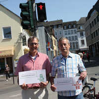 Vor dem Marx-Ampelmännchen am Simeonstiftplatz präsentieren die beiden Gewinner des Namenswettbewerbs Bernhard Schwickerath (Marxmännchen,l.) und Klaus Otto (Marxmännschi) ihre Urkunden.
