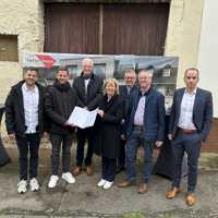 Eine Gruppe Menschen steht vor einem alten Haus. Finanz- und Bauministerin Doris Ahnen überreicht eine aufgeklappt Mappe.