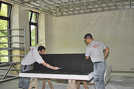 Zwei Mitarbeiter einer Spezialfirma schneiden Schallschutzplatten zu, die an einer Metallkonstruktion an der Decke befestigt werden.