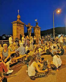 Zahlreiche Besucher eines Fests unterhalten sich im Licht einer Straßenlaterne im Sitzen und im Stehen