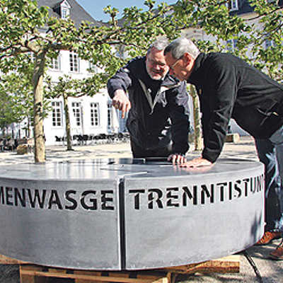 Bernd Laurenz, zuständig für den Bereich Organisation der Wallfahrt, und der Kulturbeauftragte des Bistums Micha Flesch (v. r.) überprüfen den Sockel der Skulptur auf dem Domfreihof.