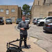 Junger Mann auf Parkplatz mit Fernbedienung und Roboter auf Rädern mit Greifarm