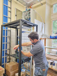 Ein Installateur in grauer Arbeitskleidung arbeitet an einem EDV-Schatlschrank