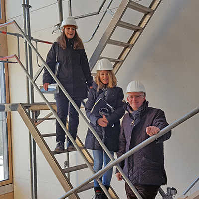 Projektleiterin Beatrix Maier und Bauleiterin Sandra Stassen (v. l.) erläutern OB Wolfram Leibe die Baufortschritte im neuen Schulgebäude (großes Foto), die man auch von außen erkennen kann.