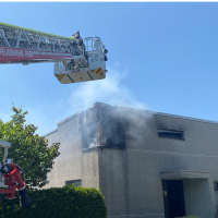 Das Bild zeigt das brennende Haus in Olewig. Von links ragt eine Drehleiter der Feuerwehr ins Bild.