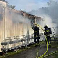 Zwei Feuerwehrleute stehen mit Schläuchen und löschen in Container. Aus diesen dringt dichter Rauch.