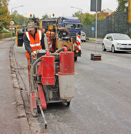 Foto: Auf der frisch aufgetragenen Fahrbahnschicht der Zurmaiener Straße begradigt ein Bauarbeiter die seitliche Kante.