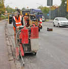 Auf der frisch aufgetragenen Fahrbahnschicht der Zurmaiener Straße begradigt ein Bauarbeiter die seitliche Kante.