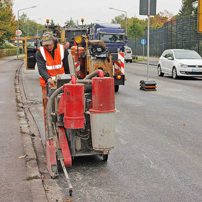 Auf der frisch aufgetragenen Fahrbahnschicht der Zurmaiener Straße begradigt ein Bauarbeiter die seitliche Kante.