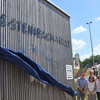 Alexander Steinbach (l.) enthüllt den Schriftzug der nach seinem Großvater benannten Halle. Sein Vater Michael Steinbach, Bürgermeisterin Elvira Garbes, Ortsvorsteher Rainer Lehnart, Innenminister Michael Ebling und OB Wolfram Leibe (v. l.) spenden Beifall. 