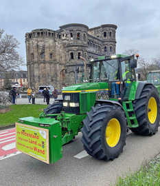 Ein grüner Traktor mit Protestbotschaft fährt vor der Porta Nigra über den Alleenring