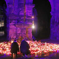 Menschen knien vor der Porta Nigra und entzünden Kerzen. Das Wahrzeichen der Stadt wird in der Dunkelheit aktuell mit der Trauerfarbe violett angestrahlt.