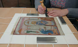 Zur fachgerechten Konservierung wird eine vielfarbige mittelalterliche Buchmalerei mit Streifen aus Japanpapier in ein Passepartout eingehängt.
