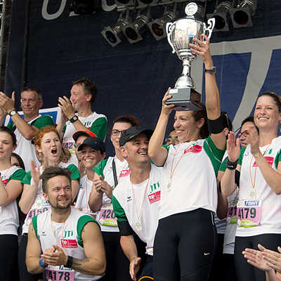 Die JTI-Läufer freuen sich über den erneuten Gewinn des Wanderpokals im Firmenlauf und feiern mit ihren Teamkollegen bei der Siegerehrung auf dem Hauptmarkt. Foto: SWT