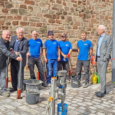 Im Beisein von OB Wolfram Leibe(r.) installieren Georg Gulla (StadtRaum Trier) und Baudezernent Andreas Ludwig (v. l.) den ersten von zehn zusätzlichen Fahrradbügeln vor der Dom-Info. Die ausführende Trierer Tiefbaufirma Wagner ist mit vier Mitarbeitern vor Ort.