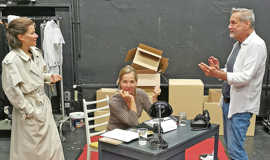 Theaterprobe mit einem Regisseur und zwei Schuaspielerinnen in einer Kulisse mit Büromöbeln