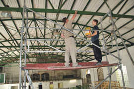 Zwei Jugendliche aus der Werkstatt in der künftigen Soccer-Halle streichen Träger der Dachkonstruktion, die renoviert wurden.