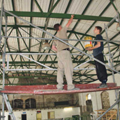 Zwei Jugendliche aus der Werkstatt in der künftigen Soccer-Halle streichen Träger der Dachkonstruktion, die renoviert wurden.