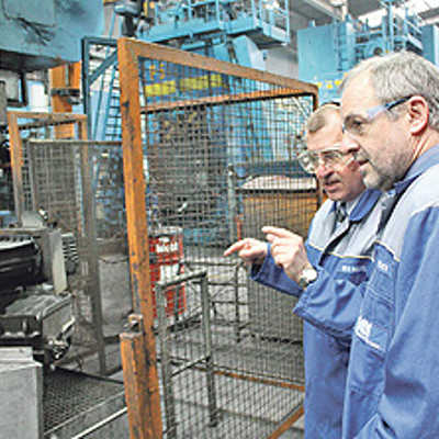 Geschäftsführer Dr. Roland Seidel zeigt Oberbürgermeister und Wirtschaftsdezernent Klaus Jensen eine riesige Presse und weitere Maschinen in den Produktionshallen.