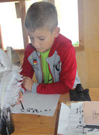 Der siebenjährige Maximilian Müller schreibt konzentriert eine Urkunde mit der Feder.
