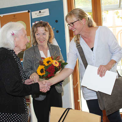 Bürgermeisterin Elvira Garbes und Regina Bruhn, stellvertretende Ortsvorsteherin in Trier-Mitte/Gartenfeld, gratulieren Justine Vicari mit einem Blumenstrauß in den Trierer Stadtfarben zum 100. Geburtstag. 