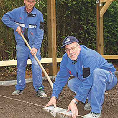 Die Stadtwerke-Mitarbeiter Elmar Herold und Karl-Heinz Maes bereiten die Pflasterarbeiten auf dem Boden des Freiluft-Klassenraums vor. Foto: SWT