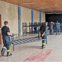 Einsatzkräfte der Trierer THW-Ortsgruppe, der Freiwilligen Feuerwehren Pfalzel und Kürenz und von der Berufsfeuerwehr tragen stapelbare Betten in die Turnhalle der Geschwister-Scholl-Schule.