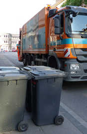Ein Müllauto steht neben mehreren Mülltonen. Im Hintergrund sieht man die Porta Nigra.