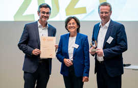 Das Jurymitglied des Solarpreises, Margit Conrad, übergibt die Urkunde und den Pokal an Carsten Grasmück und Thomas Speckter von den Stadtwerken. 