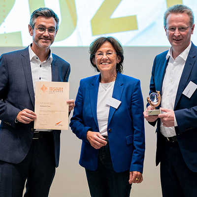Das Jurymitglied des Solarpreises, Margit Conrad, übergibt die Urkunde und den Pokal an Carsten Grasmück (l.) und Thomas Speckter von den Stadtwerken. Foto: Eurosolar