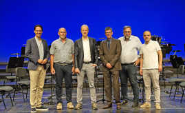 Gruppenbild: Sechs Männer stehe nebeneinander vor einem blauen Hintergrund auf einer Bühne.