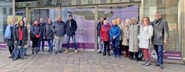Eine Gruppe von Künstlerinnen und Künstlern steht in der Simeonstraße vor dem alten Karstadt. Im Hintergrund ist eine Video-Installation des Künstlers Bodo Korsig zu sehen.