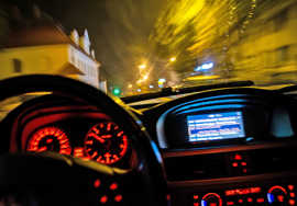 Symbolbild: Im Cockpit eines Autos leuchten die Anzeigen auf, die Straßenlaternen reflektieren auf der Windschutzscheibe und verschwimmen. 