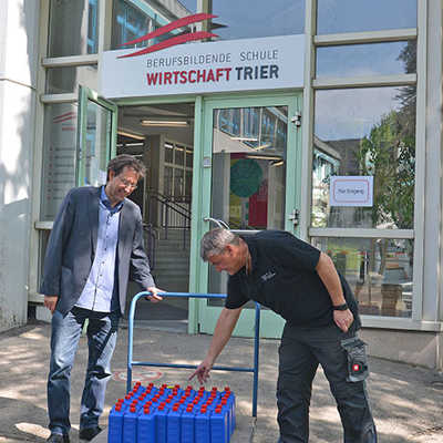 Hausmeister Wolfgang Luy kontrolliert vor der Berufsbildenden Schule für Wirtschaft Flaschen mit Desinfektionsmitteln, die Vize-Schulleiter Elgar von Klitzing entgegennimmt.