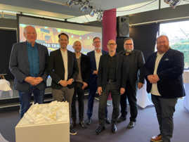 Sieben Männer haben sich zum Gruppenfoto aufgereiht. Im Vordergrund ist ein Architekturmodell des Theaters zu sehen.