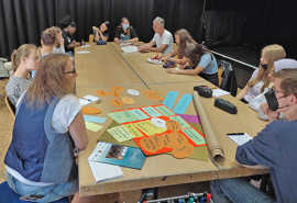 Jugendliche sitzen an einem Tisch, auf dem bunte beschriftete Karten liegen, und diskutiren