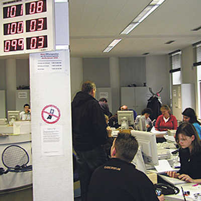 Im Schalterraum hängt eine Anzeigetafel, auf der die aufgerufenen drei Nummern links und die dazugehörigen Schalter rechts aufleuchten.