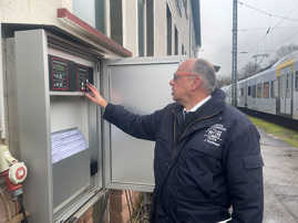 Ein Feuerwehrbeamter steht an einem Schaltkasten an einer Bahnlinie und drückt auf eine Taste