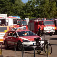 Auf einem Parkplatz stehen Einsatzfahrzeuge der Feuerwehr und des Technischen Hilfswerks bereit.