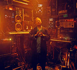 Ein Mann steht in einem Tonstudio und zeigt mit den Händen ein Herz-Symbol