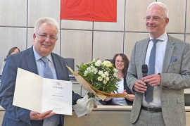 Im Rathaussaal steht Oberbürgermeister Wolfram Leibe neben Baudezernent Andreas Ludwig, der einen Blumenstrauß und seine Ruhestandsurkunde in den Händen hält.