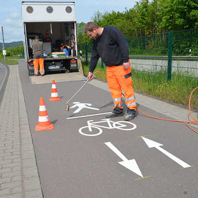 Martin Becker bringt das neue Piktogramm aus Heißplastik mit einem Gasbrenner auf den Geh- und Radweg entlang der Loebstraße auf.