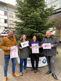 Patrick Sterzenbach, Jennifer Schaefer, Elvira Classen und Markus Nöhl stehen vor einem Weihnachtsbaum in der Innenstadt und präsentieren Plakate von „Trier ist Winterkult(ur)!“