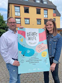Eine Frau und ein Mann zeigen das Plakat für das Selbsthilfe-Festival
