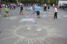 Kinder spielen auf einer Straße, die mit bunten Zeichnungen, darunter eine große Sonne, übersät ist.
