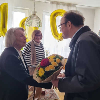 Dezernent Ralf Britten gratuliert Eleonore Freudenreich zum 100. Geburtstag mit einem Blumenstrauß in den Trierer Stadtfarben. 