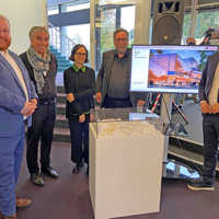 Markus Nöhl, Jörg Friedrich, Andrea Wandel, Manfred Langner und Lajos Wenzel gruppieren sich um eine Vitrine mit einem Gebäudemodell und einen Bildschirm, der eine Visualisierung für die Erweiterung des Theaters zeigt.