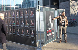 Die Plakate sind an Bauzäunen angebracht, die auf den einen Seiten großformatige Porträts von Flüchtingen zeigen und auf den anderen Seiten Banner mit Trierer Bürgerinnen und Bürgern.
